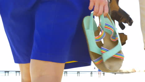 Couple-walking-on-the-beach-with-sandals-in-hands