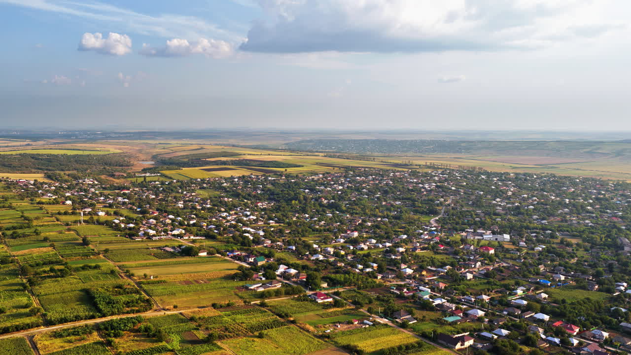 Aerial drone view of the vast Moldovan countryside with colorful patchwork fields stretching to the horizon under a partly cloudy summer sky