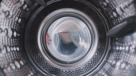 view looking out from inside washing machine as woman takes puts in white laundry load