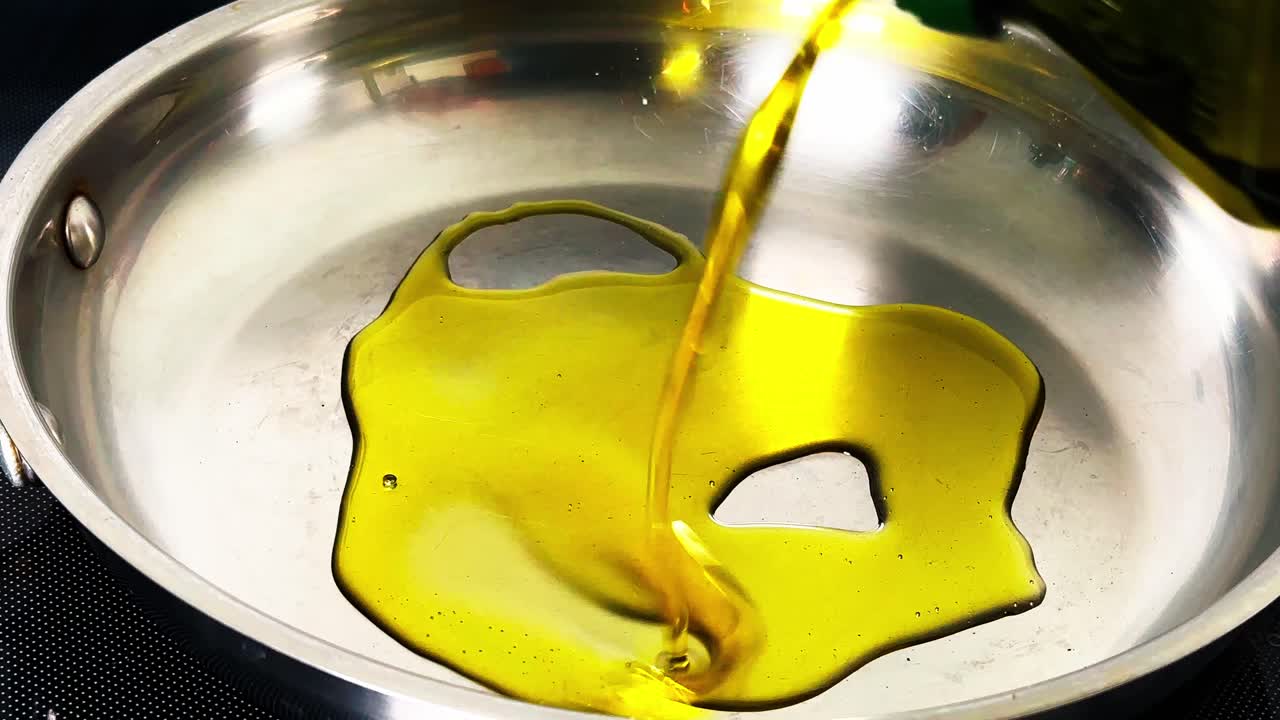Vista ravvicinata di olio extra vergine d'oliva giallo brillante versato in una padella lucida in acciaio inossidabile. Concetto di preparazione e cottura del cibo