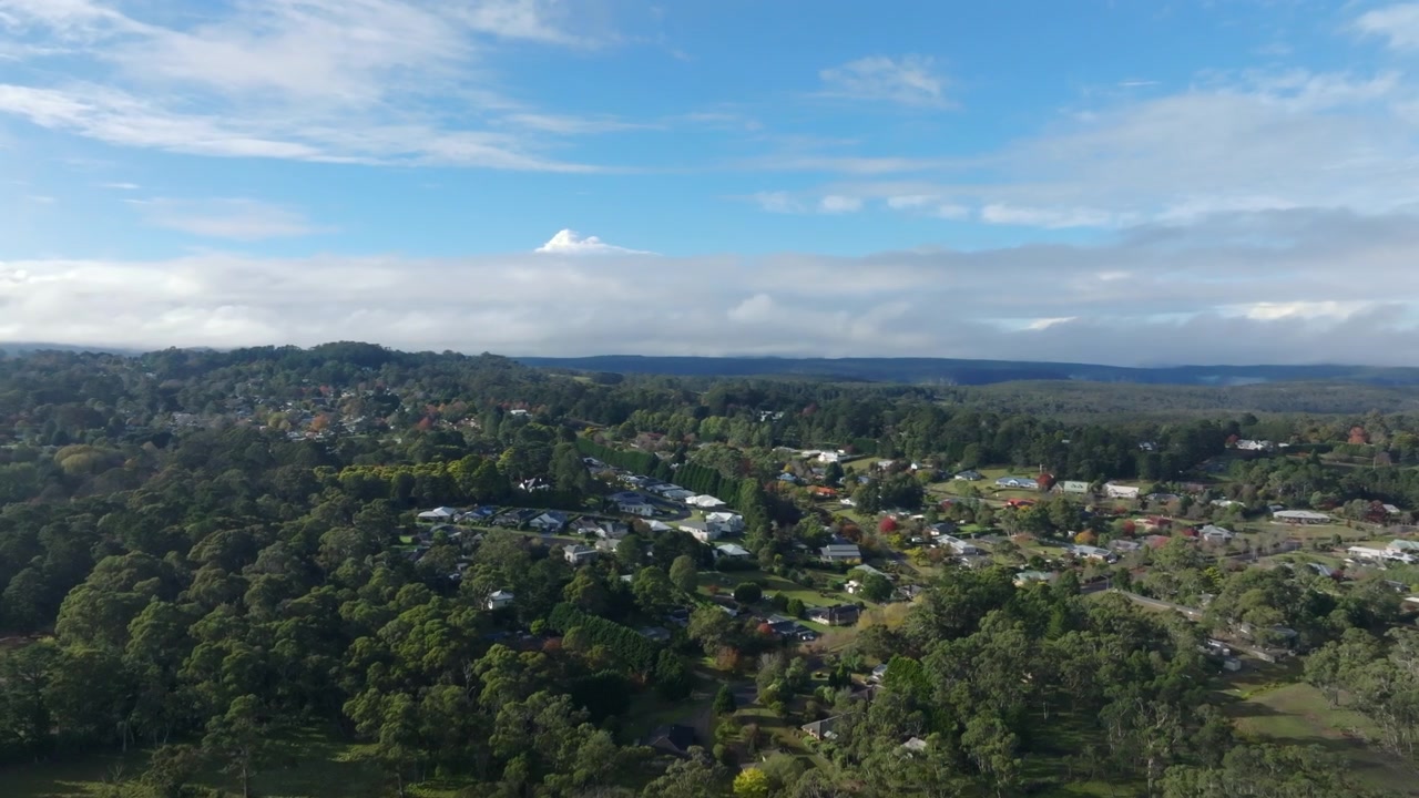 Ampia ripresa aerea con drone che rivela Bundanoon annidata tra boscaglia ondulata e foreste sotto nuvole estese nelle Southern Highlands, Nuovo Galles del Sud, Australia