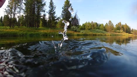 lassen sie einen magneten zum magnetfischen in zeitlupe in einen fluss fallen und beobachten sie das plätschern und blasen, während der fischer auf der flussperle nach schätzen sucht