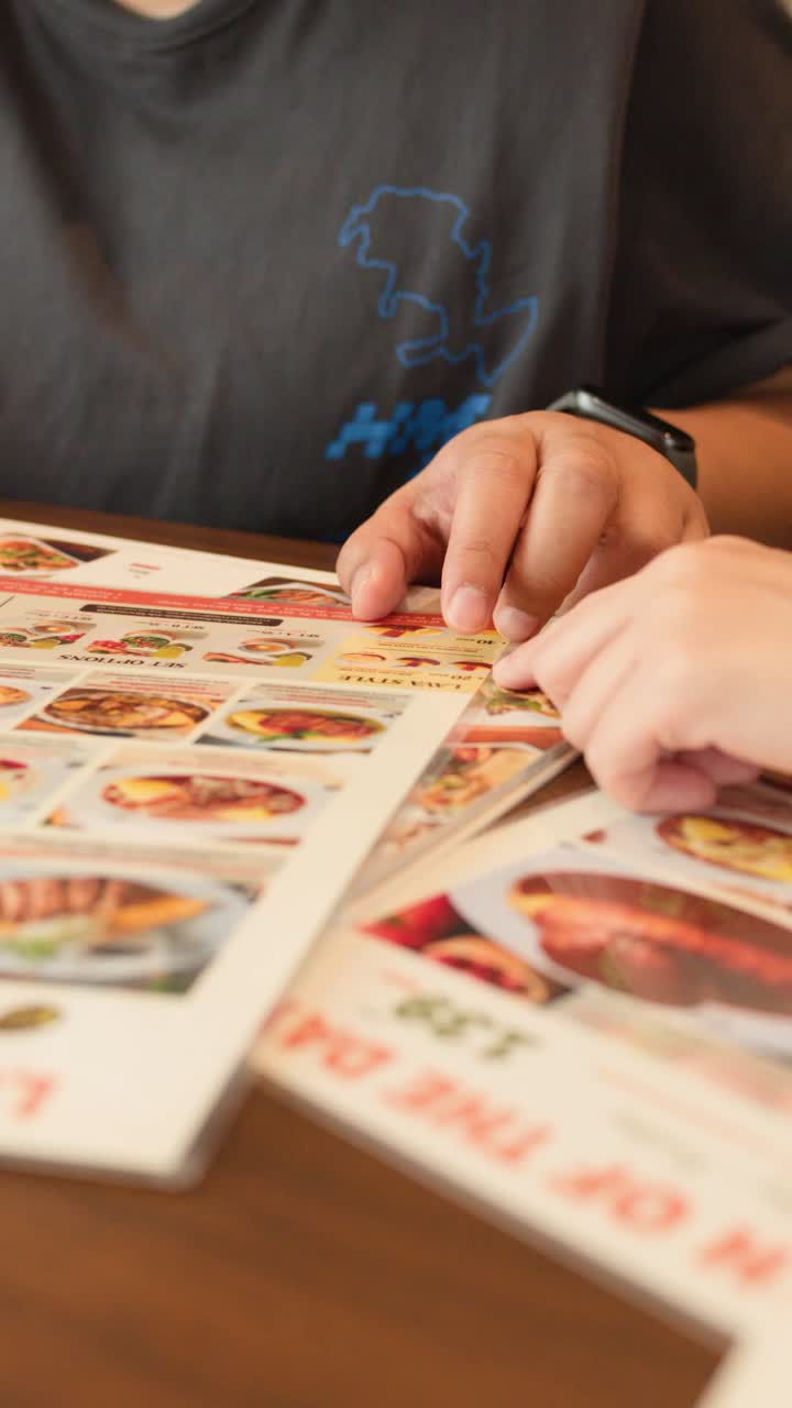 To personer peger og diskuterer madmuligheder på en menu ved et restaurantbord i Bangkok.