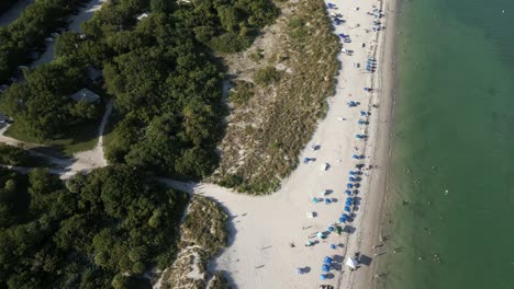 Cape-Florida-Llighthouse-south-end-of-Key-Biscayne-in-Miami-Dade-County,-Florida-USA-aerial-footage-of-people-sunbathing-on-beach