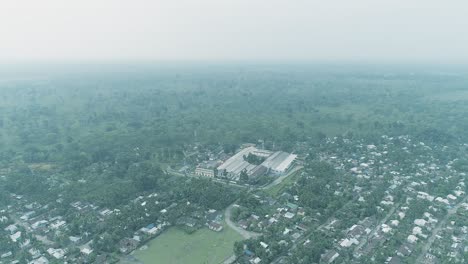 Aerial-view-over-beautiful-village-surrounded-by-trees-of-tropical-forest-on-a-large-field-on-a-misty-day