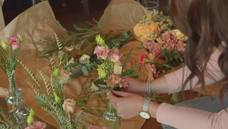 woman with long brown hair decorating flower bouquets, back handheld view