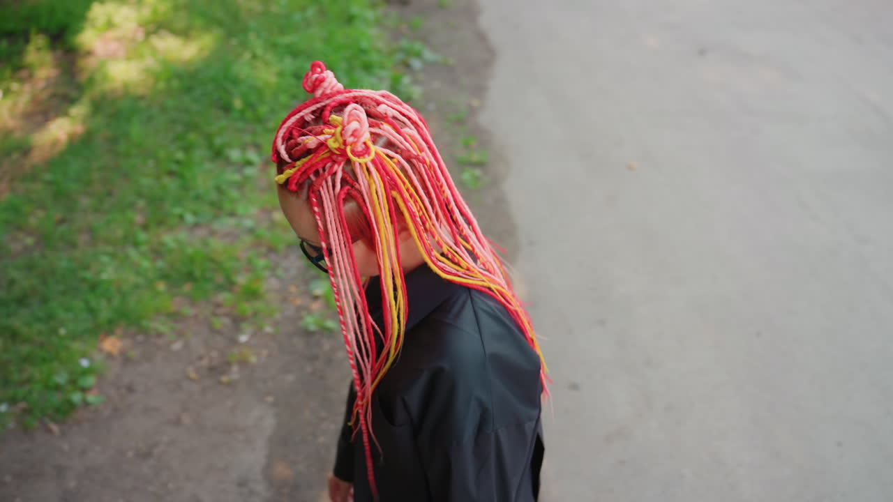Primeros planos cenitales y en ángulo de una mujer con rastas llamativas sentada en un banco, cabeza gacha, manos cerca de la cara, expresión pensativa, camino del parque y texturas de madera desgastada visibles, luz solar suave