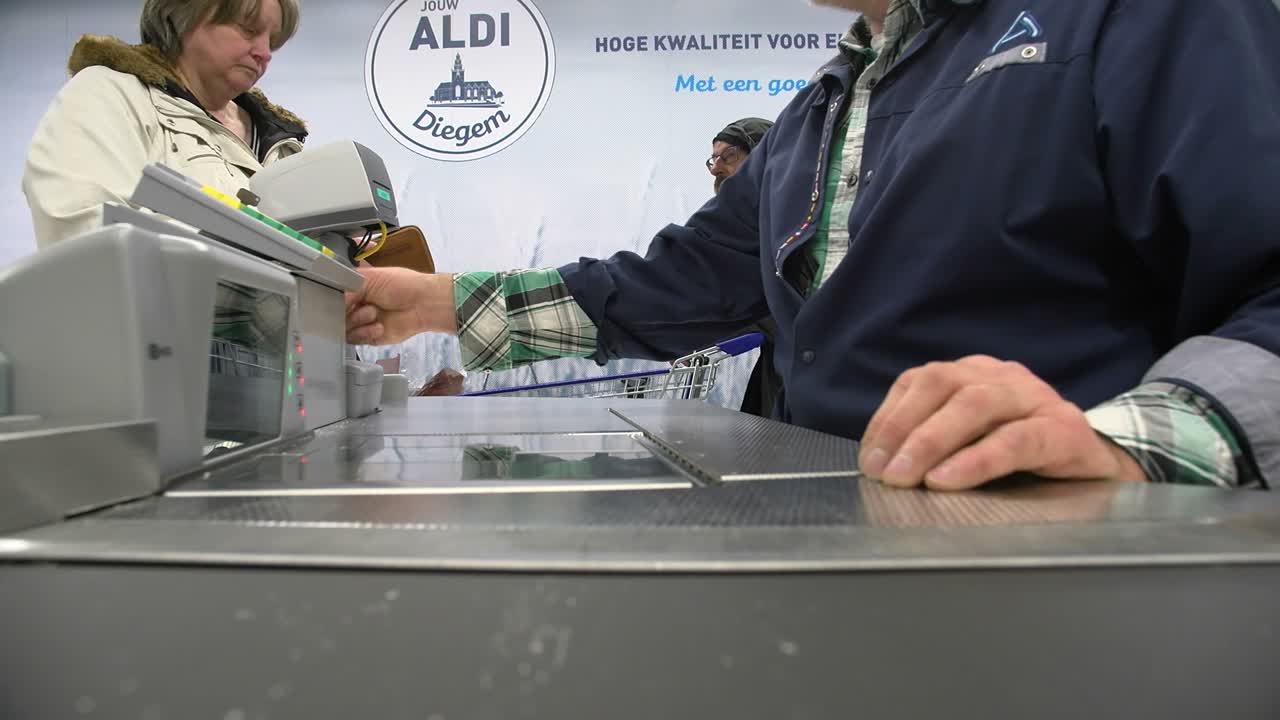 Moving POV on conveyer belt in supermarket with paying customers. Cashier scans the camera like a real product. Wide vertical tracking shot.