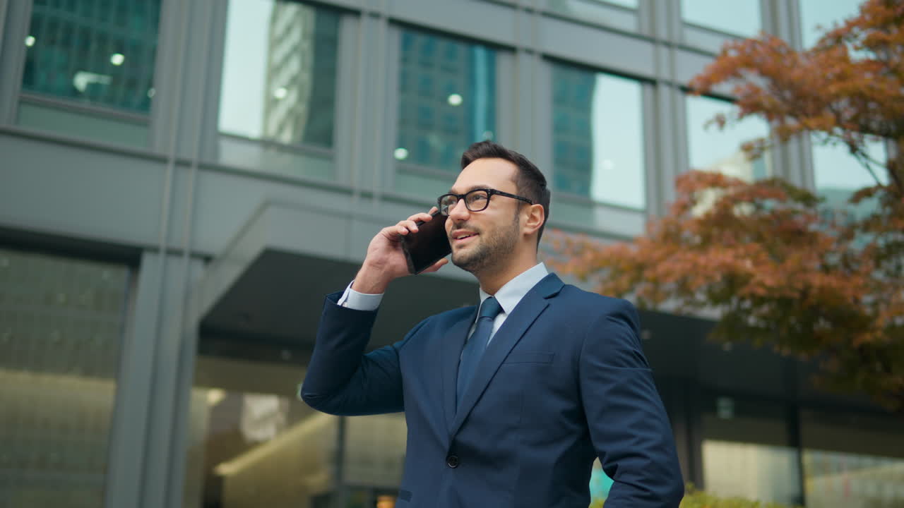 hombre de negocios feliz hablando por teléfono de pie afuera contra el edificio corporativo - paralaje en cámara lenta