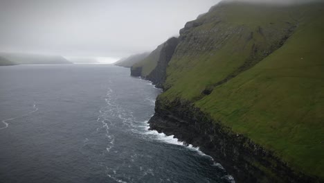 dramatic cliffs rise steeply above a vast ocean, with fog rolling in to create a moody atmosphere in kalsoy, faroe islands, showcasing the raw and untouched beauty of nature, drone orbiting