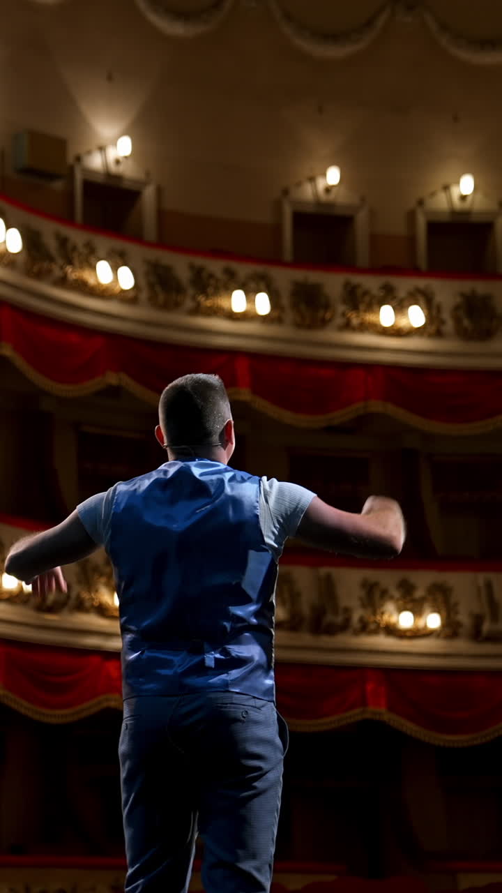Actor bowing on theatrical stage. Man is standing on the scene of the classical theater and acting his role during the rehearsal before the empty hall. Back view. Vertical video