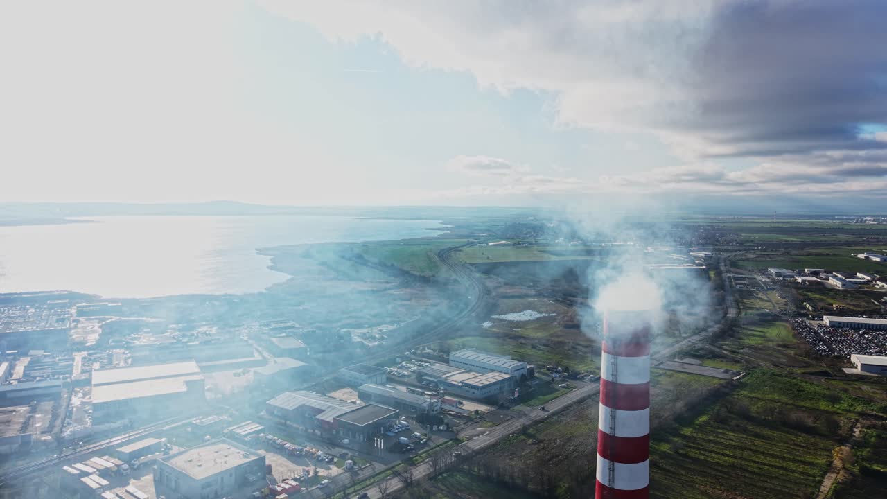 Smoke rises from a factory near water on a cloudy day