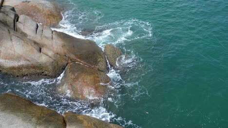 static shot of a rocky beach with water splashing foaming on the edge of the rocks