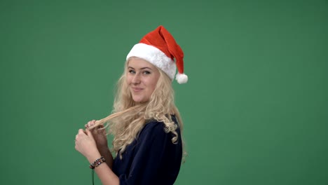 joven rubia con una gorra roja de navidad sonriendo y jugando con el cabello, pantalla verde clave de croma