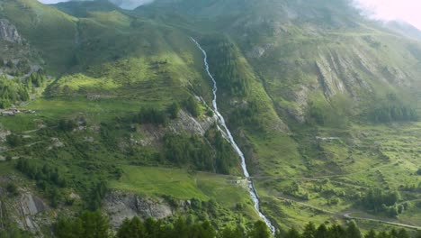 aerial view of a river running down through the green mountains of the alps