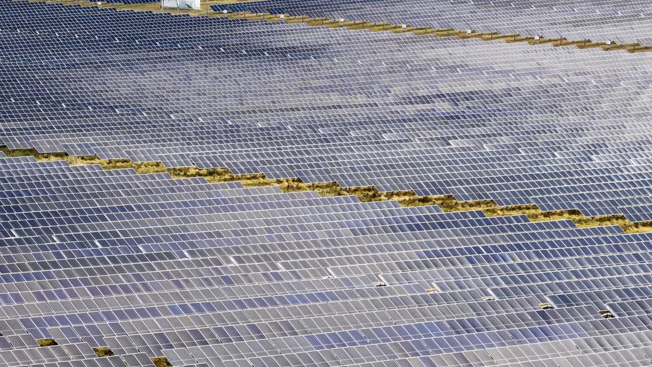 Drone glides above expansive solar panel array, bright daylight, wide view, clean energy focus