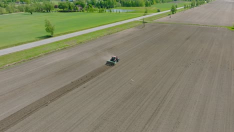 Aerial-view-of-plowed-field-with-tractor-sowing-seeds-of-wheat,-agricultural-theme,-farm-tractor-and-seeder-planting-crops-on-a-field-on-sunny-spring-day,-birdseye-drone-shot-moving-forward