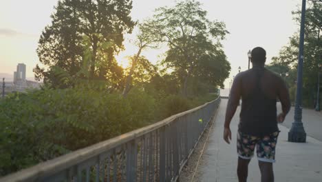 Black-Male-in-Fancy-Street-Clothes-Walking-Away-from-Screen-Along-Empty-Path-In-Barcelona,-Spain-at-Sunrise-in-6K