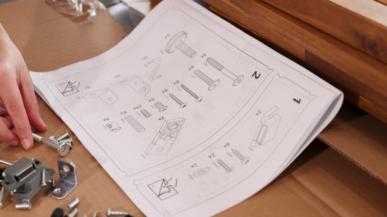 Hands assembling furniture using instructions and tools on a wooden surface. Bright lighting highlights detailed assembly process