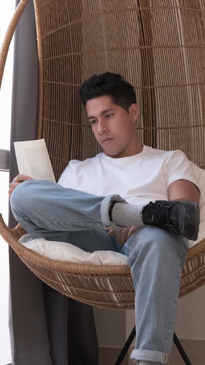 Portrait of young man reading a book while sitting in a comfortable chair at home.