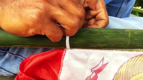 la mano de un hombre está atando una cuerda de bandera en un palo de bambú