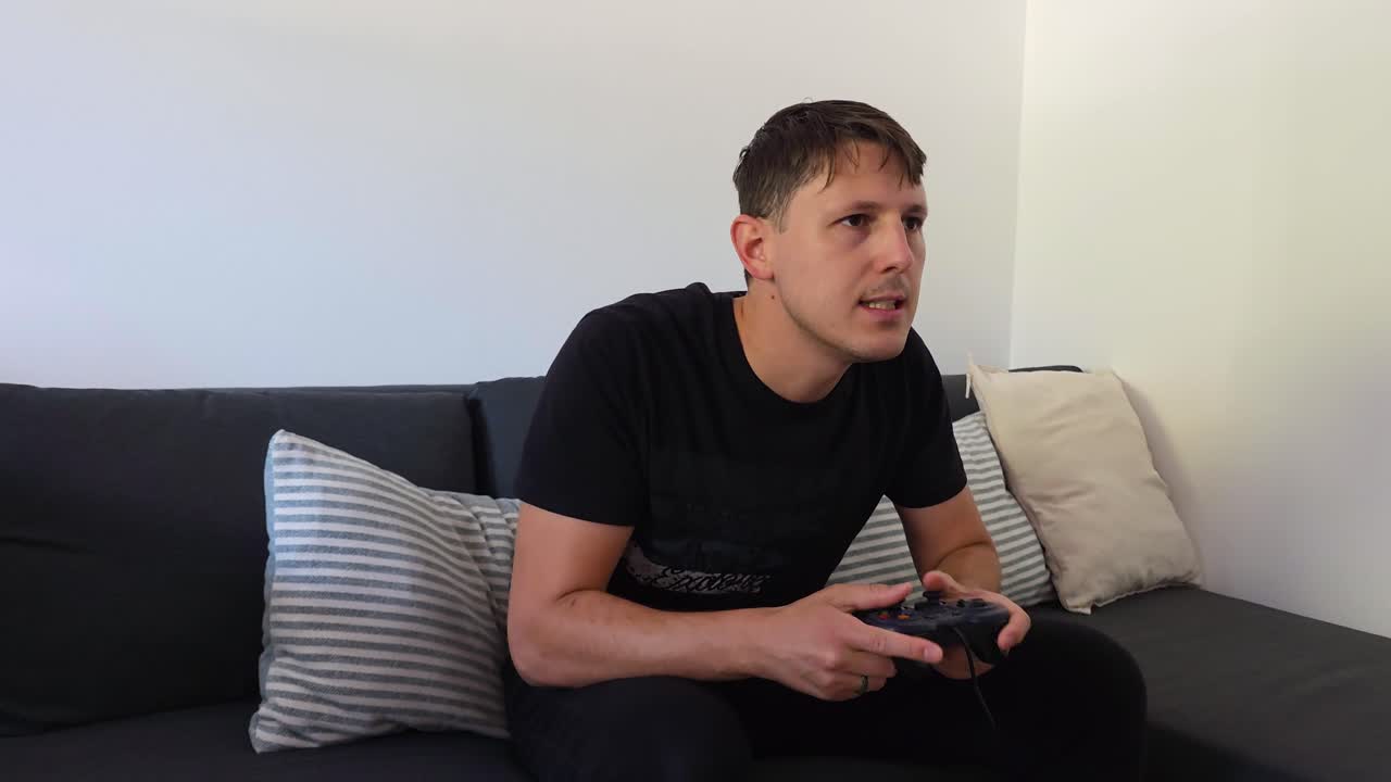 Gamer leans forward on couch with eyes locked on screen, fingers flying on controller signaling a very intense gaming session. Static medium shot