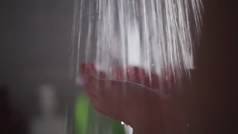mujer disfruta de agua caliente sosteniendo las manos bajo una corriente fuerte. dama lavándose las manos en un baño oscuro. mujer tomando el sol bajo agua caliente en una ducha oscura