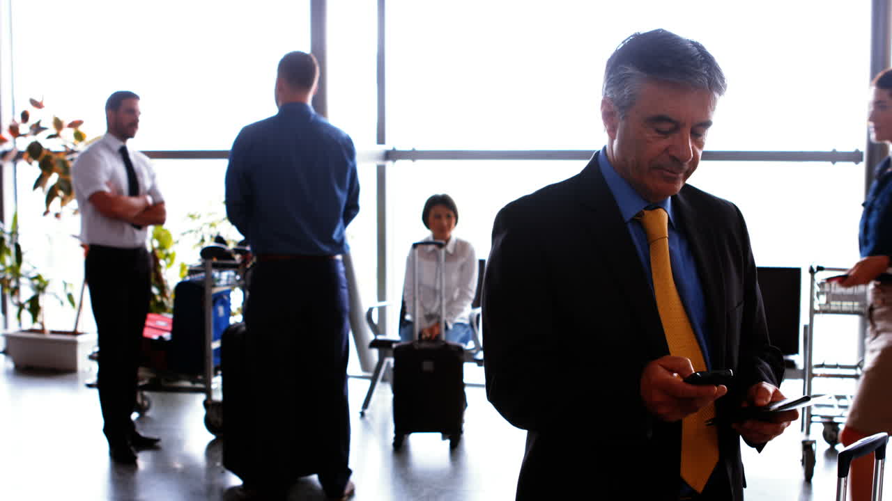 hombre de negocios usando el teléfono móvil mientras los viajeros interactúan entre sí