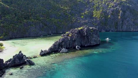 tourist filipino boat docked next to a jagged limestone mountain and crystal clear waters of tapiutan island bay