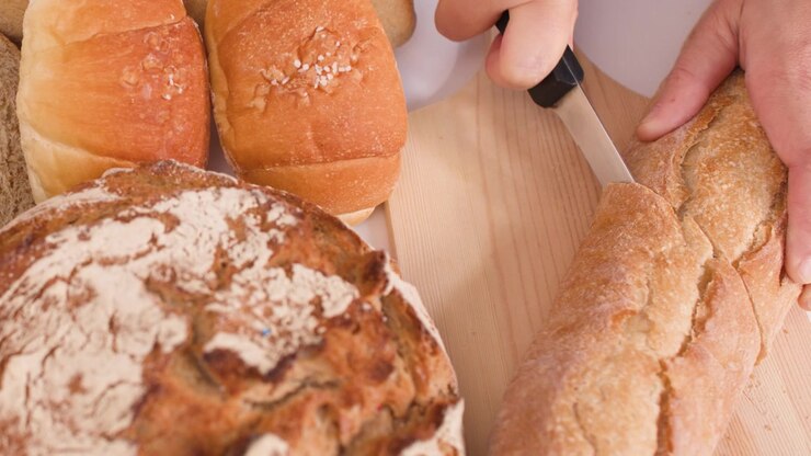 Person Slicing Fresh Crusty Baguette on Wooden Cutting Board