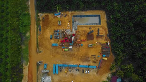 toma cinematográfica de drones de perforación en tierra y estructura de plataforma de reacondicionamiento y equipo de plataforma para exploración y explotación de petróleo en medio de la jungla rodeada de palmeras durante la puesta de sol