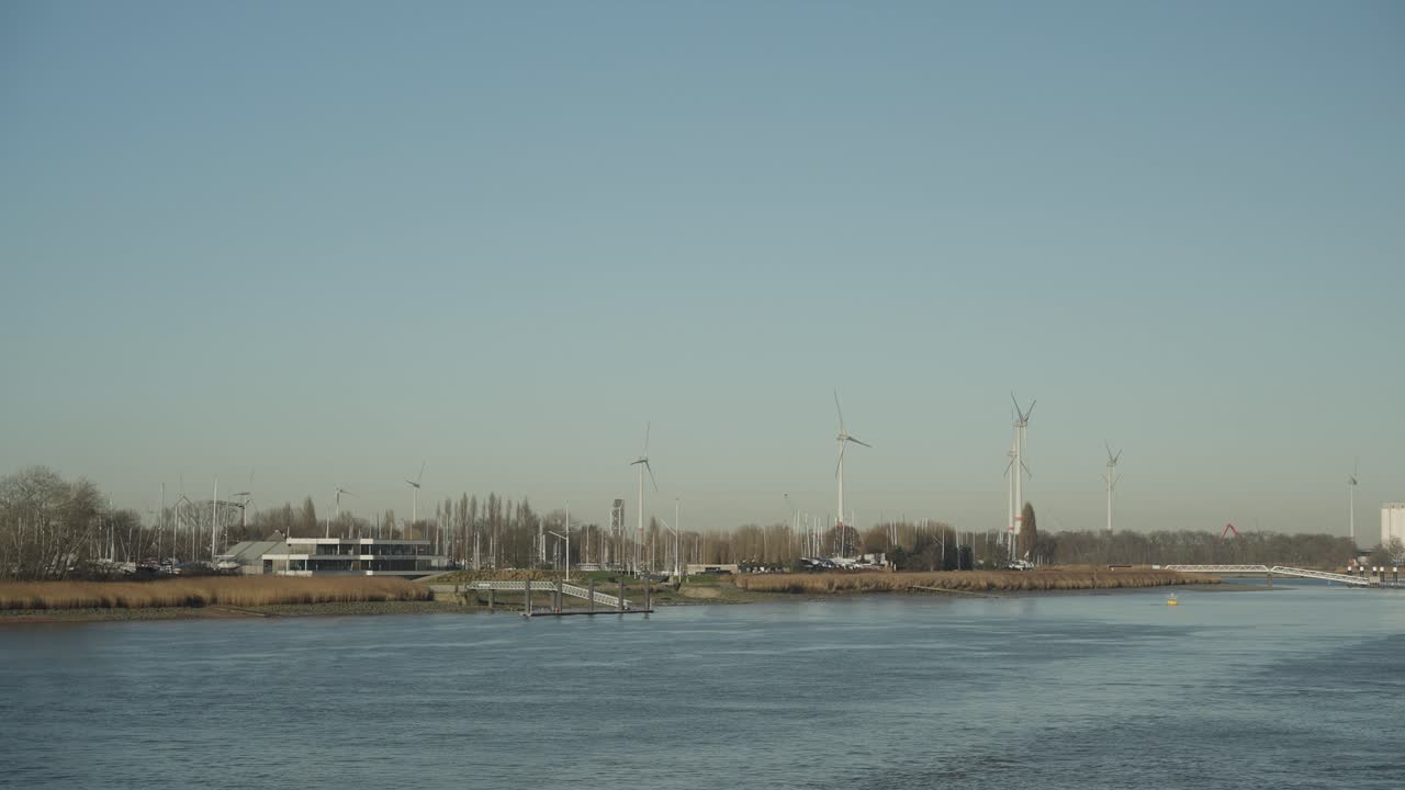 강 근처의 풍력 터빈에 의해 재생 가능한 녹색 에너지가 만들어지고 있습니다.