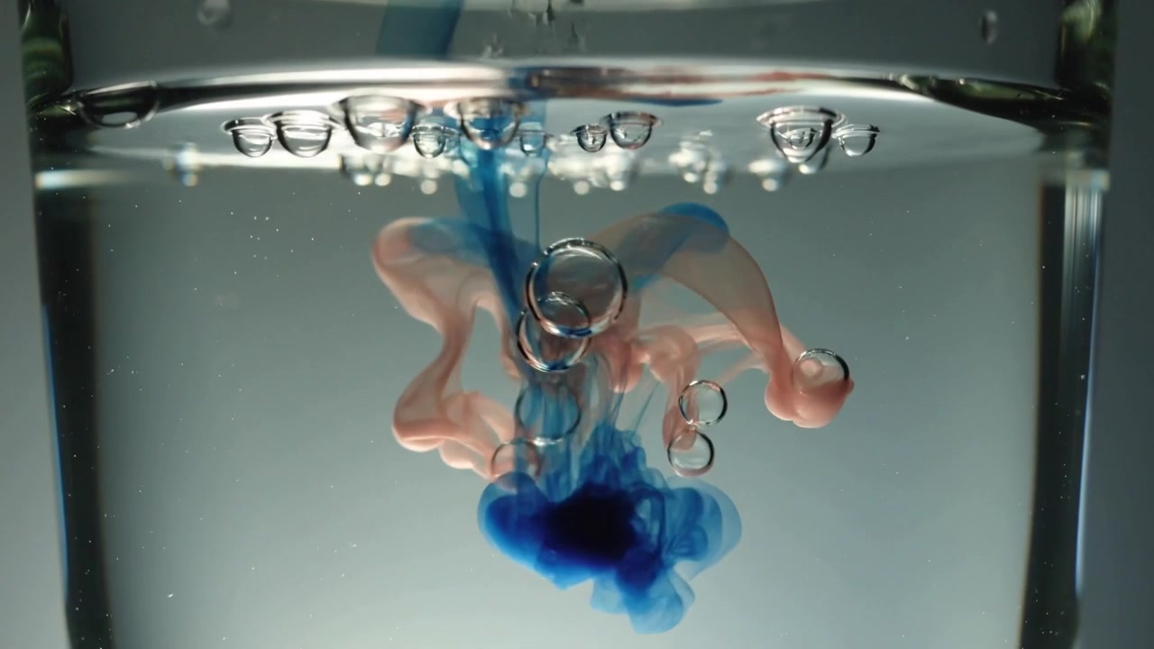 Corriente de tinte azul entrando y formando un bulbo en un vaso de precipitados, mostrando mezcla con penachos rosados y burbujas ascendentes