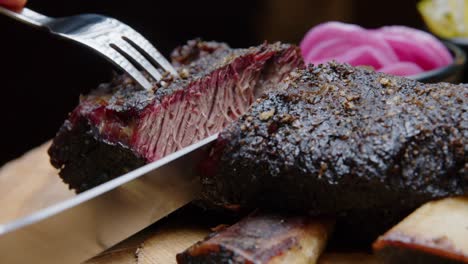 the chef cuts barbecue ribs with a fork and knife to show the perfectly cooked meat - close-up