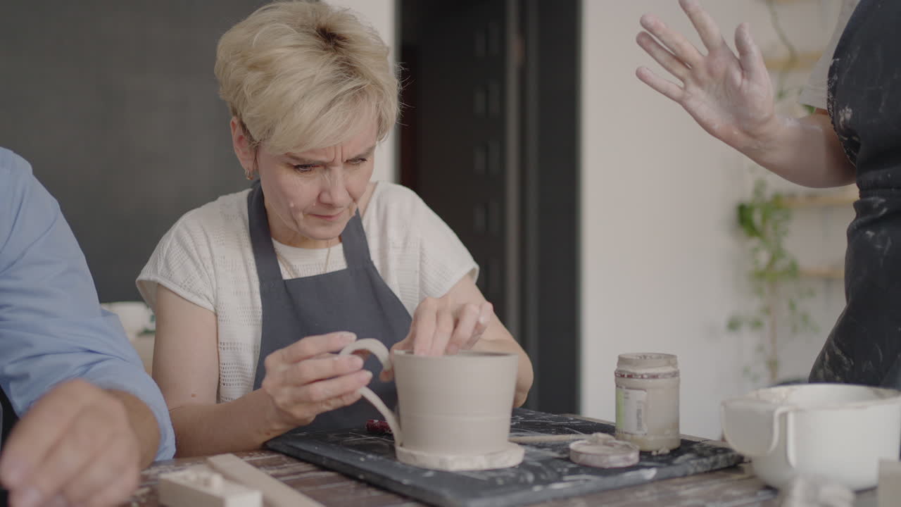 Three elderly people work on a potter's wheel in slow motion