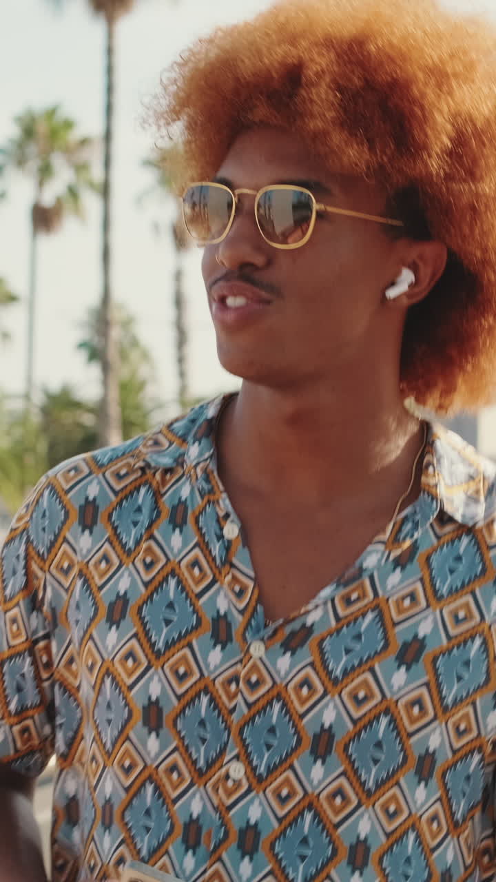 Giovane uomo con capelli afro e occhiali da sole che ascolta musica all'aperto