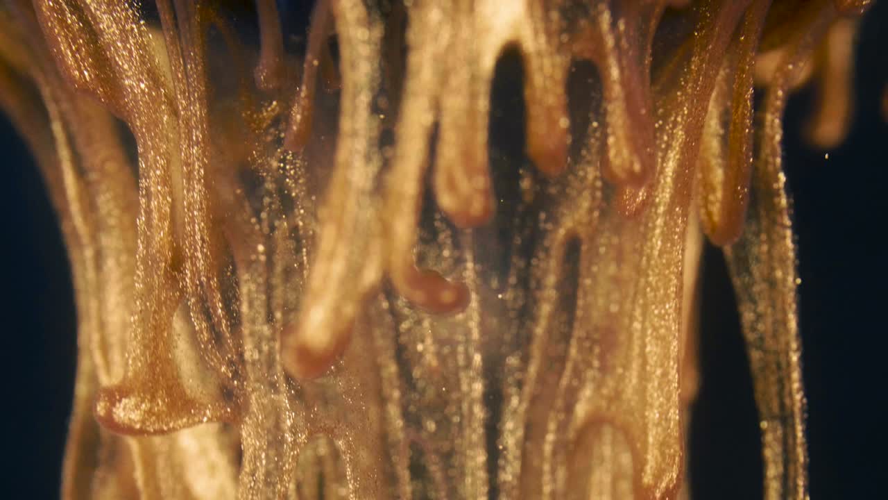 황금 잉크 입자는 검은 바탕에 다채로운 혼란으로 물에 흐른다.