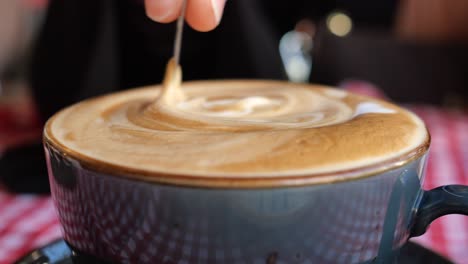 close-up of a hand stirring latte art in a coffee cup