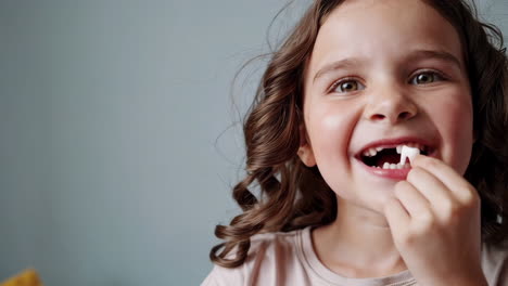 a happy young girl smiles, showing a missing front tooth and playing with a fake tooth prop