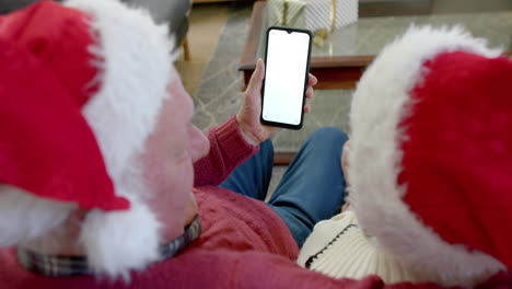 Pareja-Caucásica-Mayor-Con-Sombreros-De-Santa-Con-Teléfono-Inteligente-Con-Espacio-Para-Copiar-En-Navidad,-Cámara-Lenta