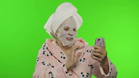 Grandmother-in-bathrobe,-face-mask.-Old-woman-making-selfies-using-mobile-phone