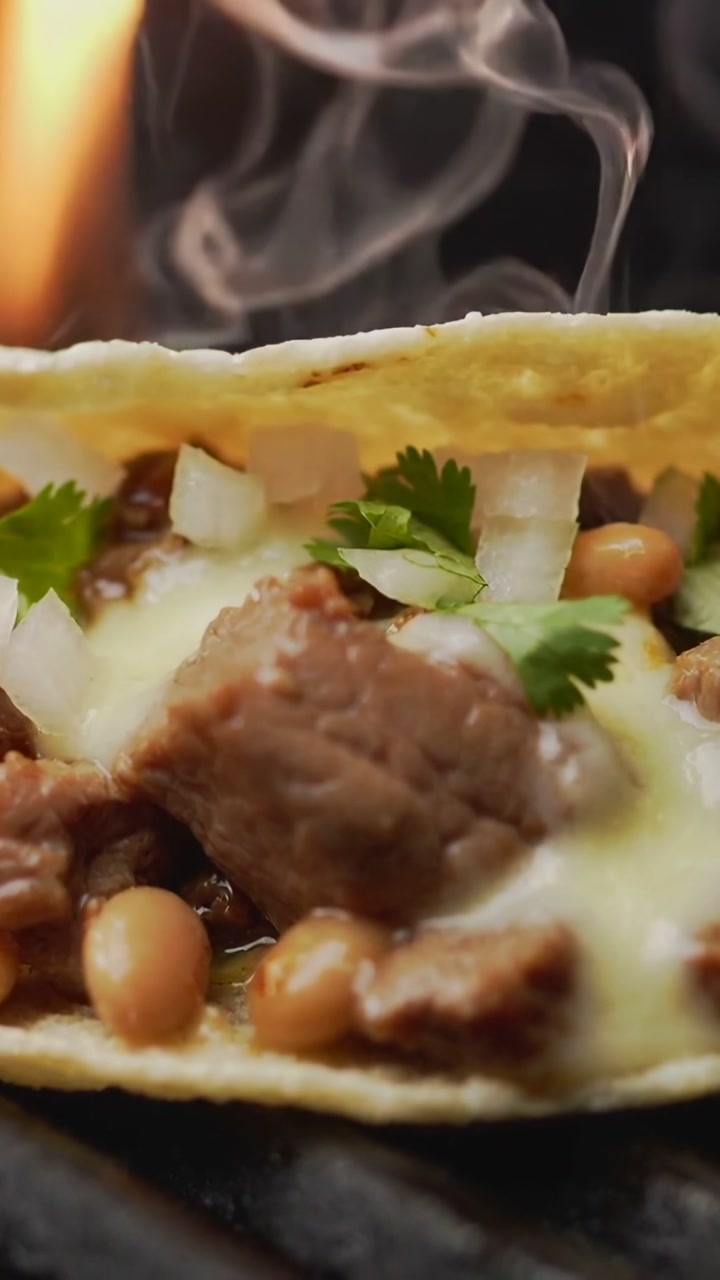 Vertical video: Igniting flame heating corn tortilla taco on griddle, melting cheese over beef