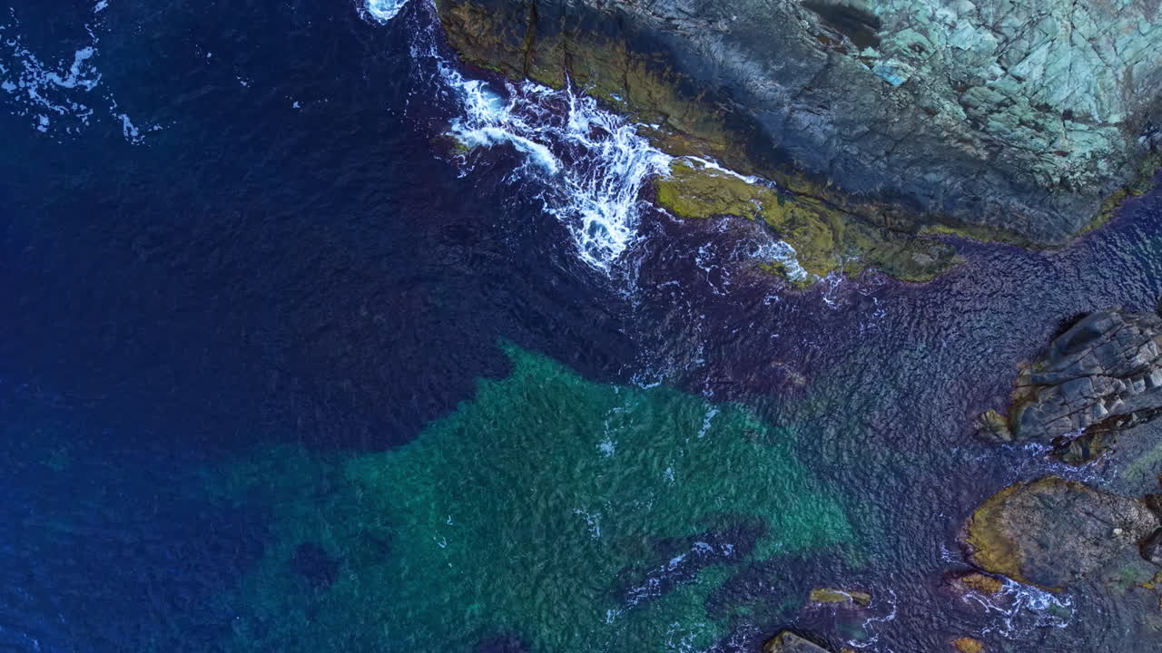 Colors of the ocean dance at the rocky shore as waves embrace the land under the warm sunlight of a clear summer afternoon
