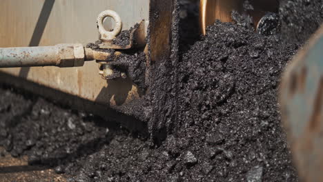 close-up of hot asphalt pouring out the paver machine to the road. asphalt paver machine during road construction. heavy truck laying out black bitumen.