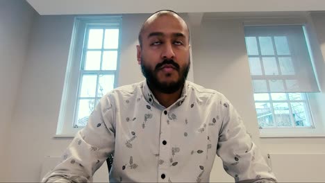 Asian-Indian-male-sitting-down-at-office-looking-at-computer-screen