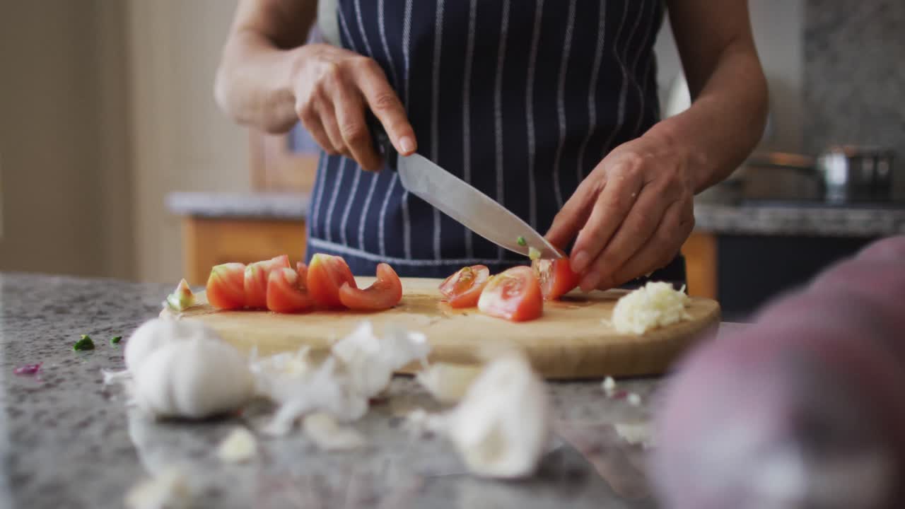 Mid section of caucasian senior woman wearing aprons chopping vegetables in the kitchen at home