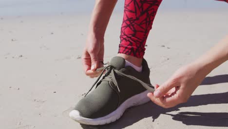 Caucasian-woman-tying-her-shoe-on-the-beach-and-blue-sky-background