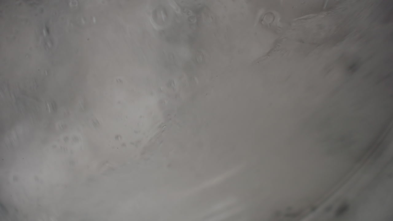 Close up laundry machine window with soapy water and cloth swirling, frothy foam, steamy condensation on glass, blurred motion during cleaning cycle inside modern laundromat
