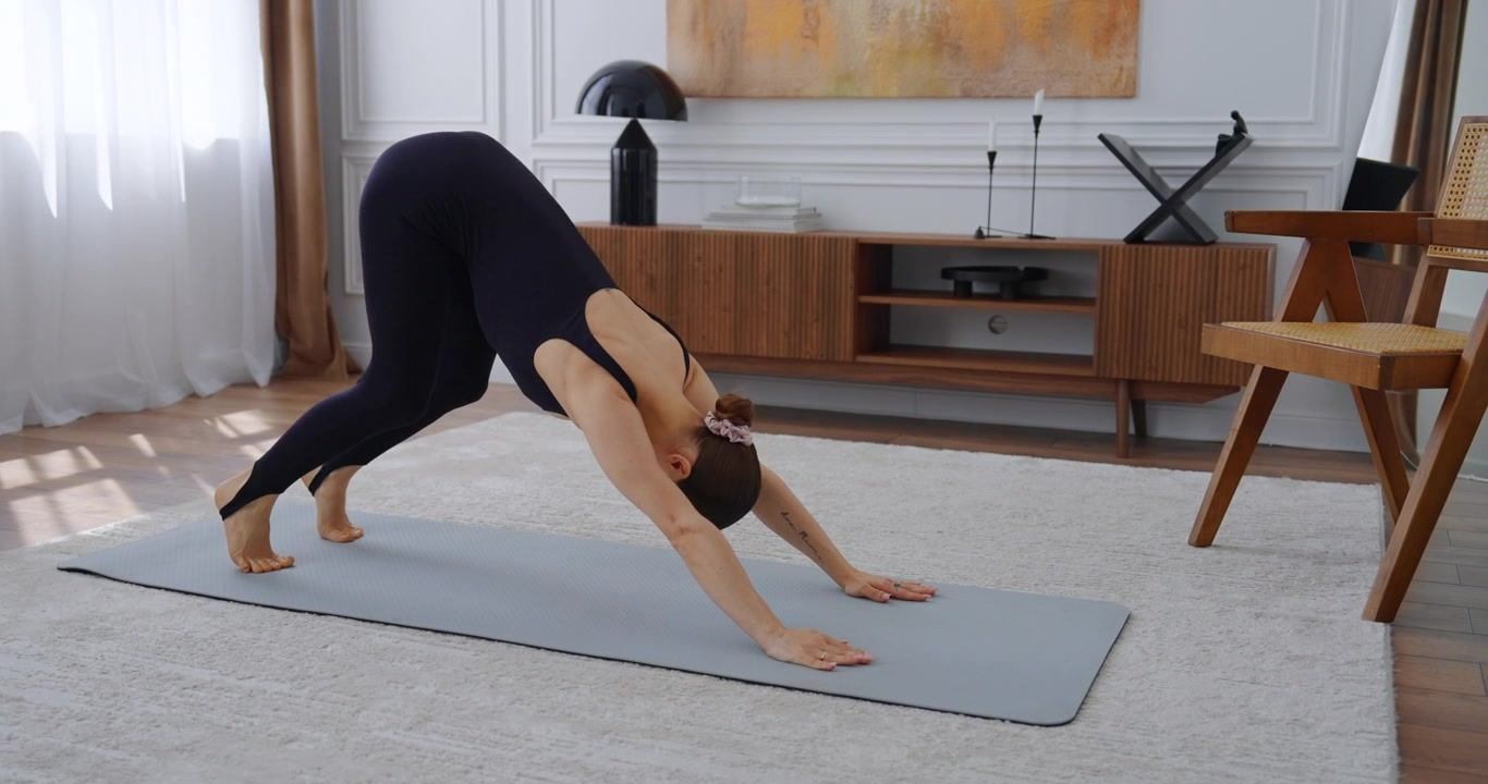 Junge Frau praktiziert Yoga-Posen auf einer Matte zu Hause