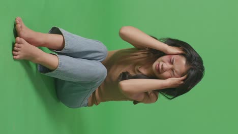 full body of young asian woman victim of violence with bruise on body having nervous breakdown and screaming while sitting in the green screen background studio